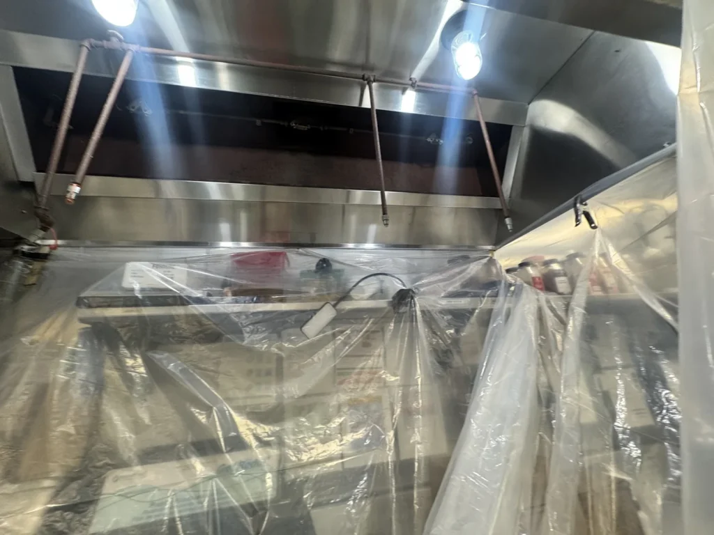 Kitchen equipment covered with protective sheeting beneath an open hood